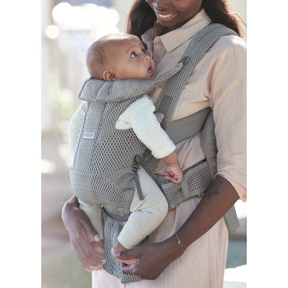 Mother wearing BABY BJORN Baby Carrier Free in gray mesh, cradling baby securely against her chest.