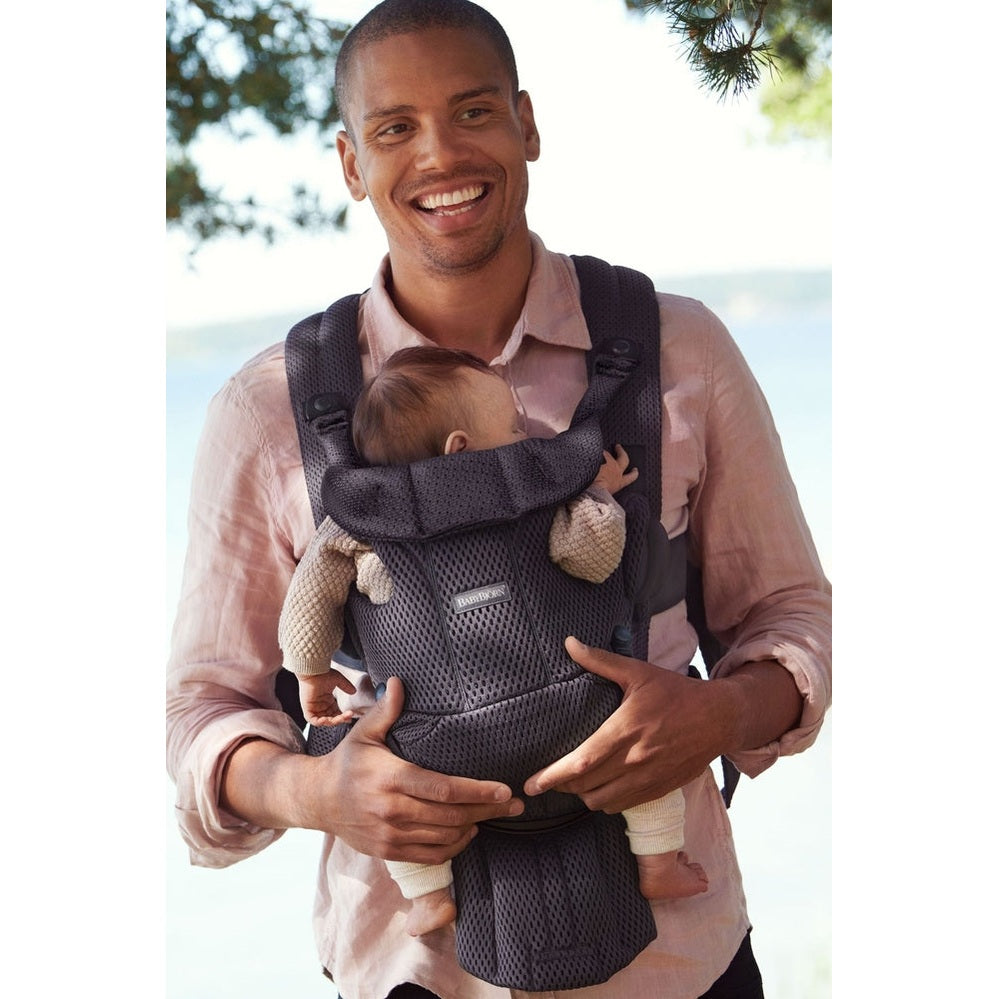 Father outdoors wearing the BABYBJORN Baby Carrier Free in dark gray, securely carrying a baby facing inward.