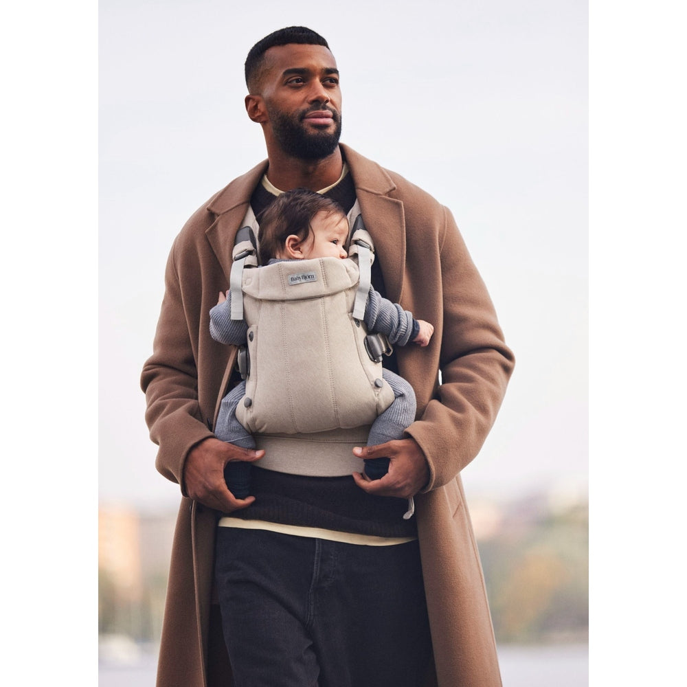 BabyBjorn Baby Carrier Harmony beige front-facing infant secured on dad's chest with sturdy straps.