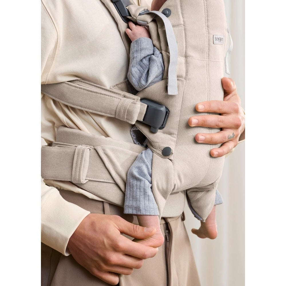 BabyBjorn Baby Carrier Harmony in beige worn by parent with secured waist belt and buckle, baby snug inside.