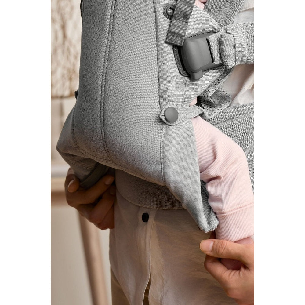 BabyBjorn Baby Carrier Harmony in gray being adjusted by caregiver, securing the leg opening and strap.