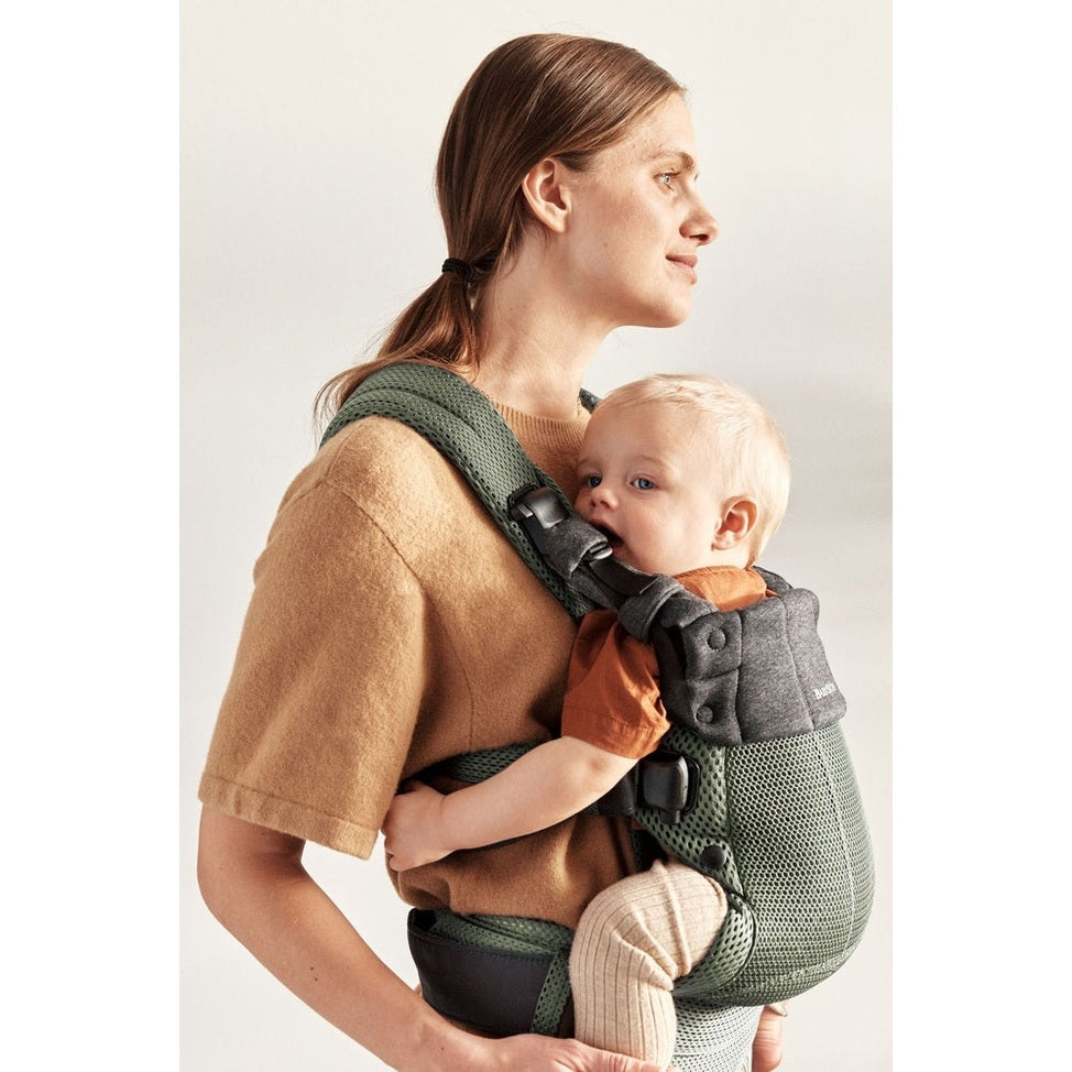 BabyBjorn Harmony baby carrier in green mesh worn by mother with buckled straps, baby facing chest.