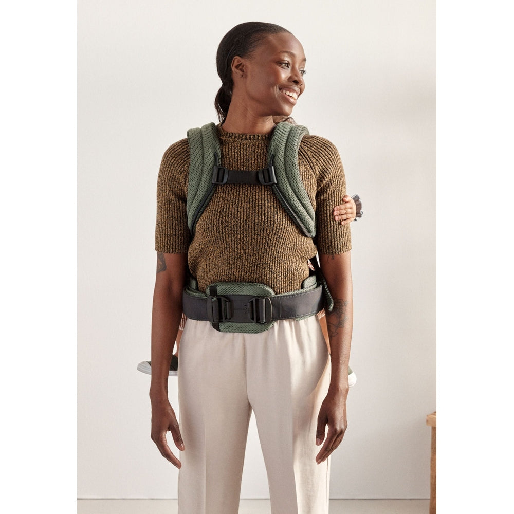 BabyBjorn Harmony baby carrier worn by smiling adult, green padded straps and secure waist belt shown.