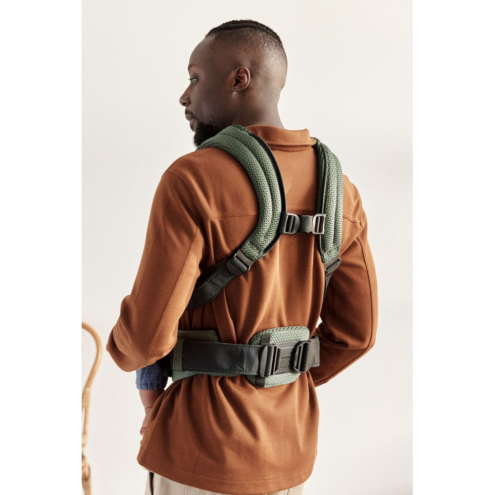 BabyBjorn Baby Carrier Harmony in green with padded straps and hip belt, worn by a man carrying a baby on his back.