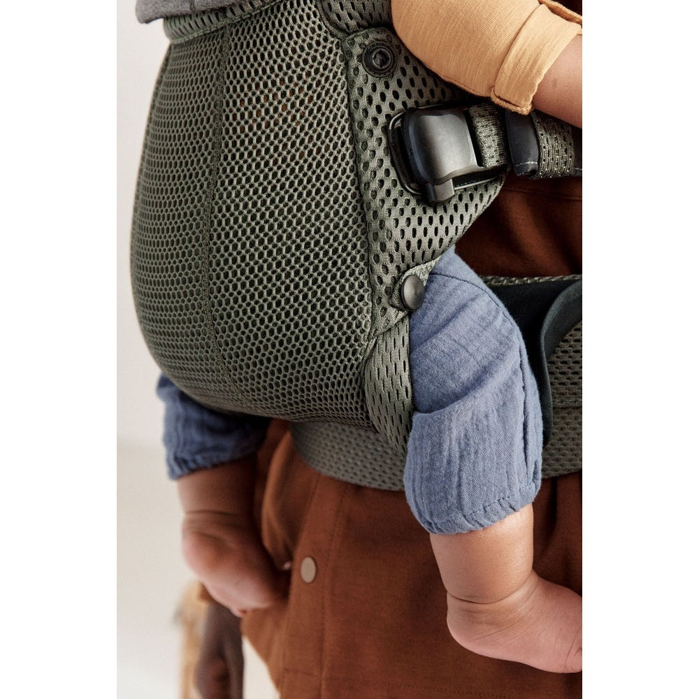 BabyBjorn Baby Carrier Harmony in olive mesh, worn by caregiver with secure buckle and snug seating.