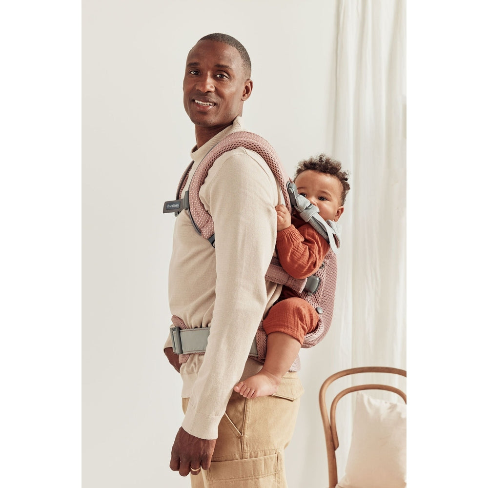 Parent wears BabyBjorn Baby Carrier Harmony in pink mesh, carrying baby on back with supportive waist belt.