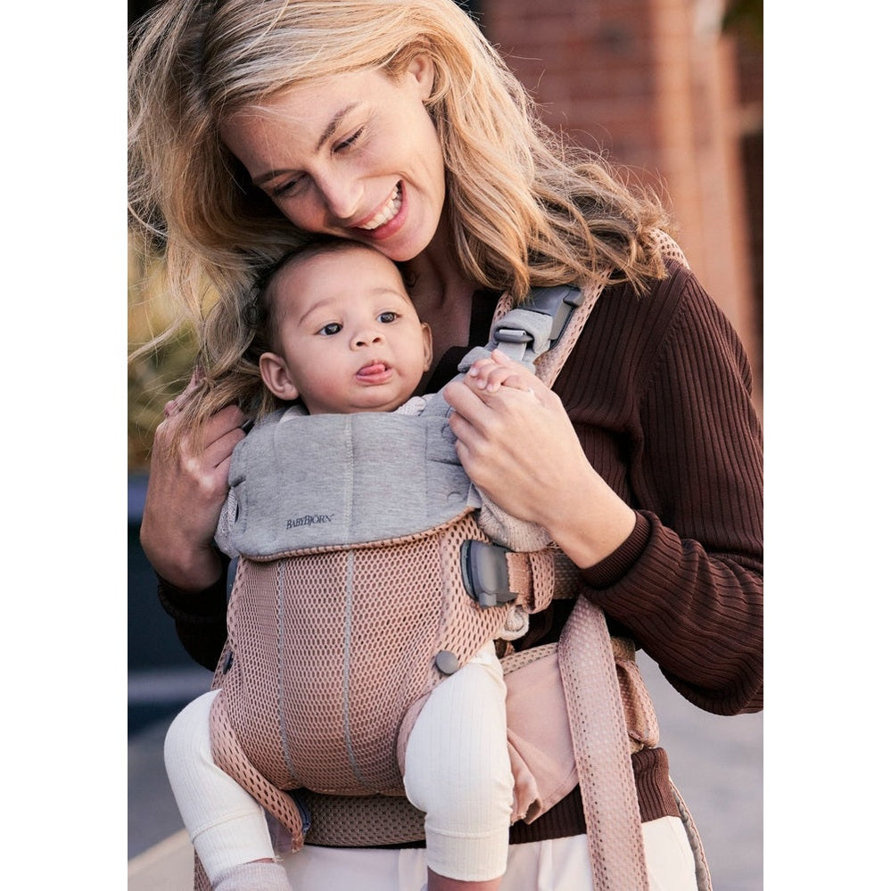 BabyBjorn Baby Carrier Harmony in blush mesh; smiling mom holds baby securely in the buckled front carrier.