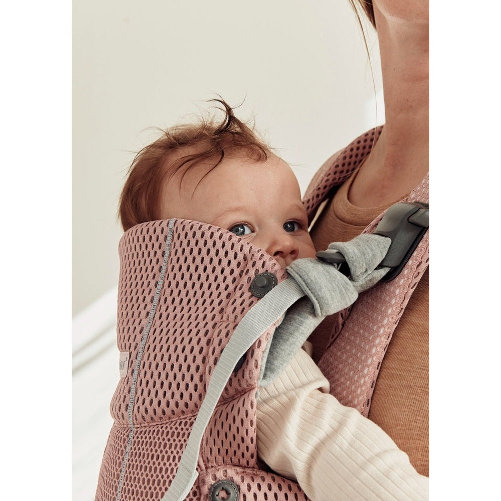 BabyBjorn Harmony baby carrier in pink mesh, showing a baby snug against caregiver with a secure gray buckle.
