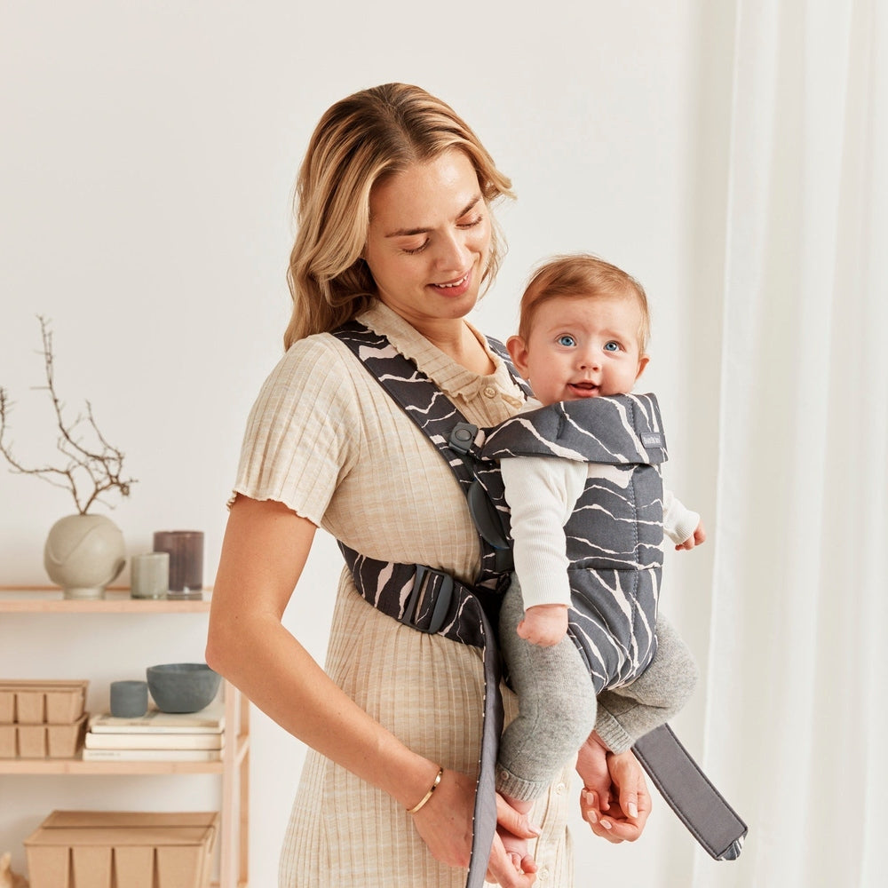 BabyBjorn Bouncer Bliss Black Mesh Bundle with Baby Carrier Mini Landscape Holiday Bundle: mother securely carries smiling baby in dark mesh carrier.