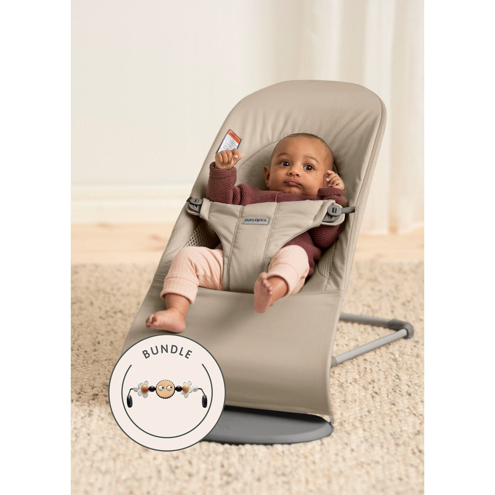BabyBjorn Bouncer Bliss in beige, baby secured in the reclined harness on a sturdy stand, bundle badge visible.