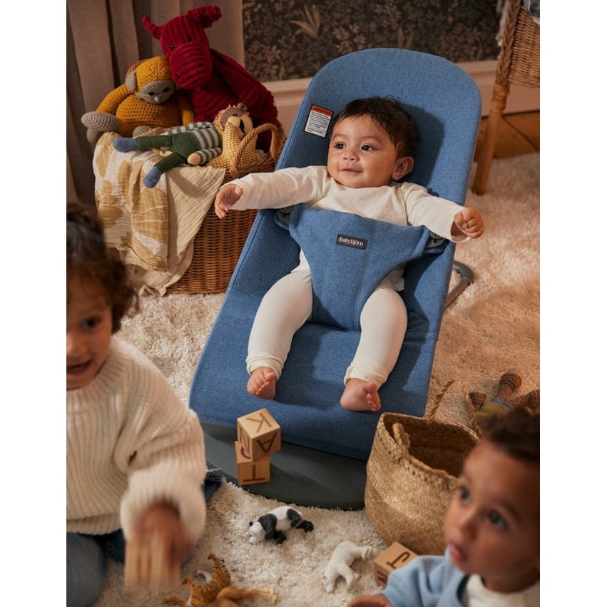 BabyBjorn Bouncer Bliss blue fabric baby rocker with a baby sitting upright and arms out, toys nearby.