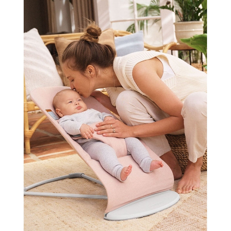 BabyBjorn Bouncer Bliss pink fabric infant bouncer; mother tenderly kisses baby resting in the curved cushioned seat.