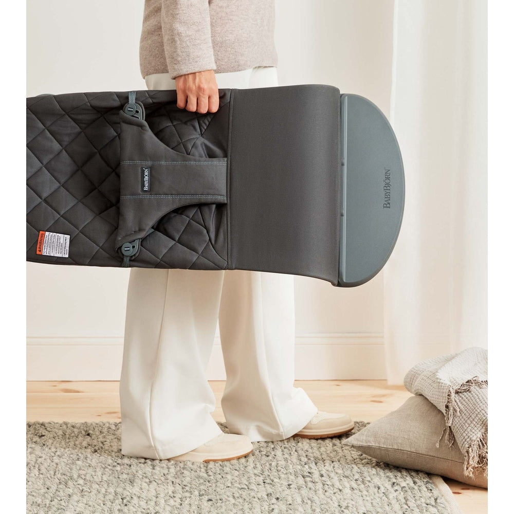 BABYBJORN Bouncer Bliss in dark gray, folded with quilted cover, carried by parent for easy transport.