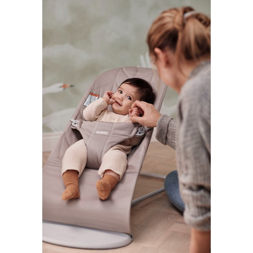 BabyBjorn Bouncer Bliss infant bouncer in soft beige; caregiver gently adjusts straps as baby smiles.