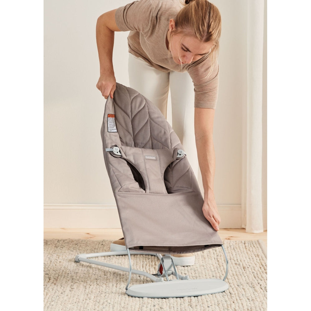 Person assembling the BabyBjorn Bouncer Bliss in gray fabric, featuring a curved metal frame and secure seat.