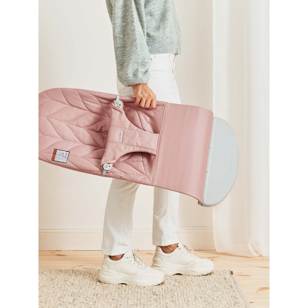 BabyBjorn Bouncer Bliss pink, being carried by a person with the folded seat and carry handle visible.