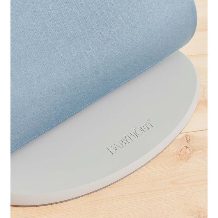 BabyBjorn Bouncer Bliss blue fabric seat atop a gray circular base on a wooden floor.