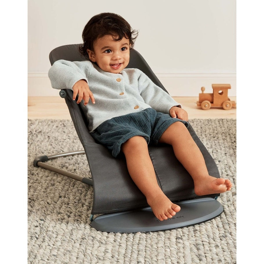 BabyBjorn Bouncer Bliss by BABY BJORN in dark gray fabric, baby smiling in the rocker with a metal base.