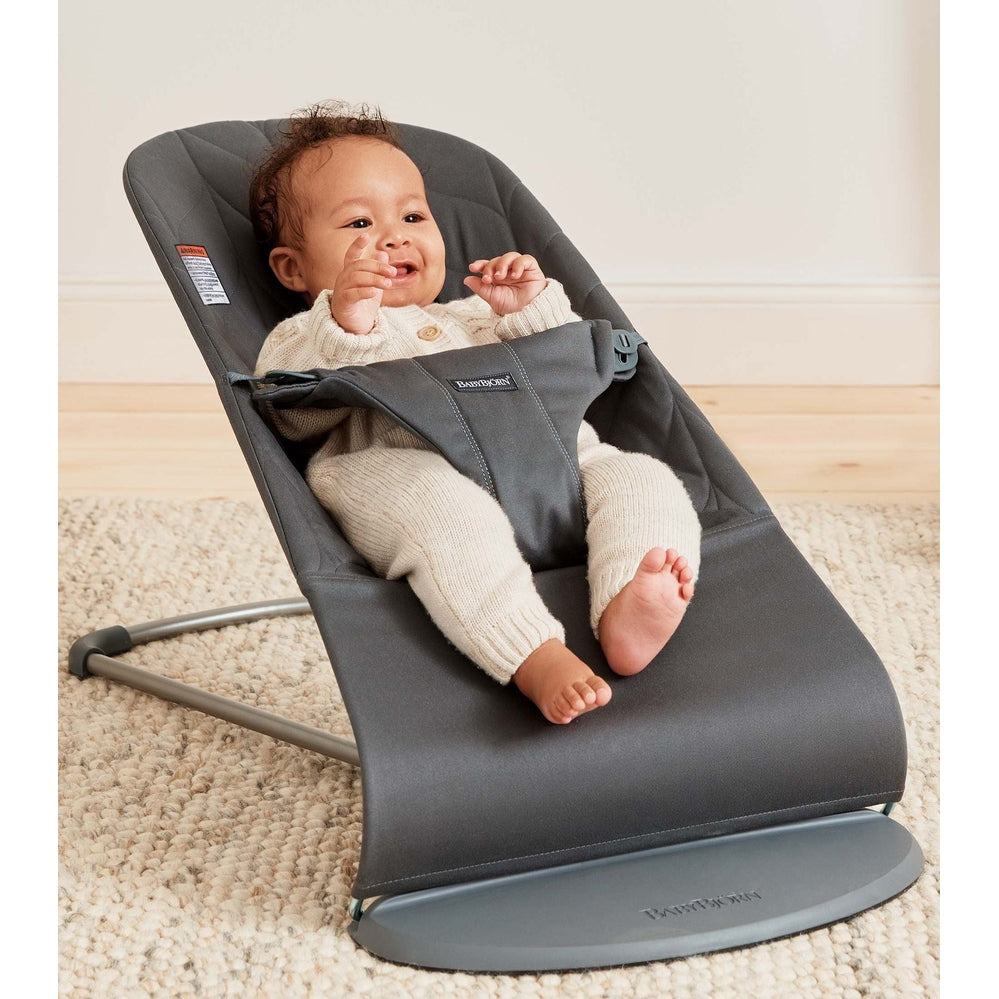 BabyBjorn Bouncer Bliss gray fabric, baby buckled and smiling in the reclined rocker.