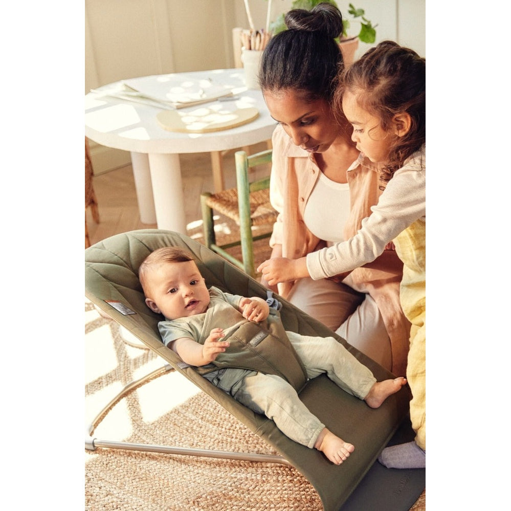 BabyBjorn Bouncer Bliss in green; baby reclines secured in harness while caregiver smiles nearby.