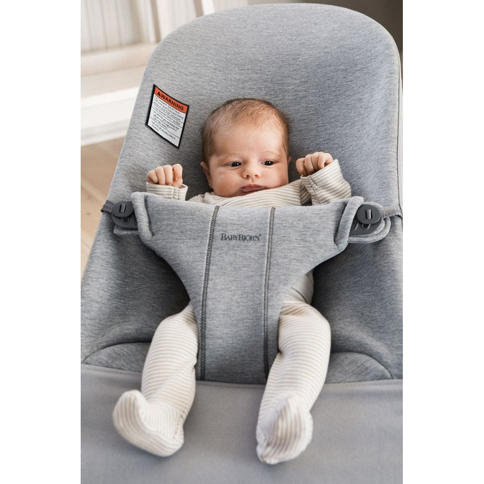 BABYBJORN Bouncer Bliss in gray with padded sides and secure harness as a baby sits upright with arms raised.