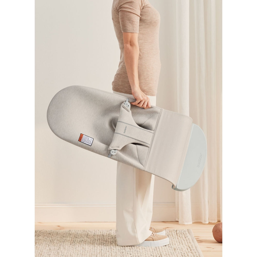 BABY BJORN Bouncer Bliss in soft gray, folded and carried indoors to highlight its compact design.