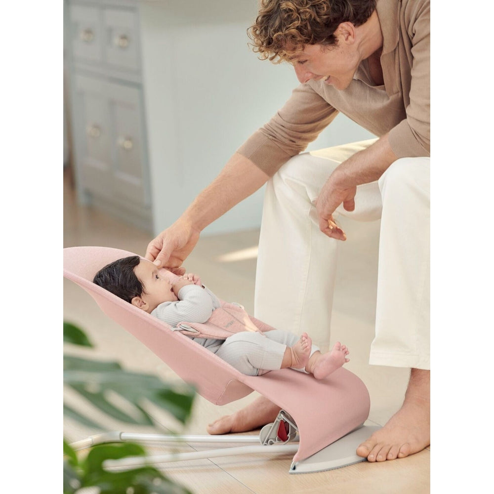 BabyBjorn Bouncer Bliss pink infant bouncer; parent softly touches baby's face as infant reclines.