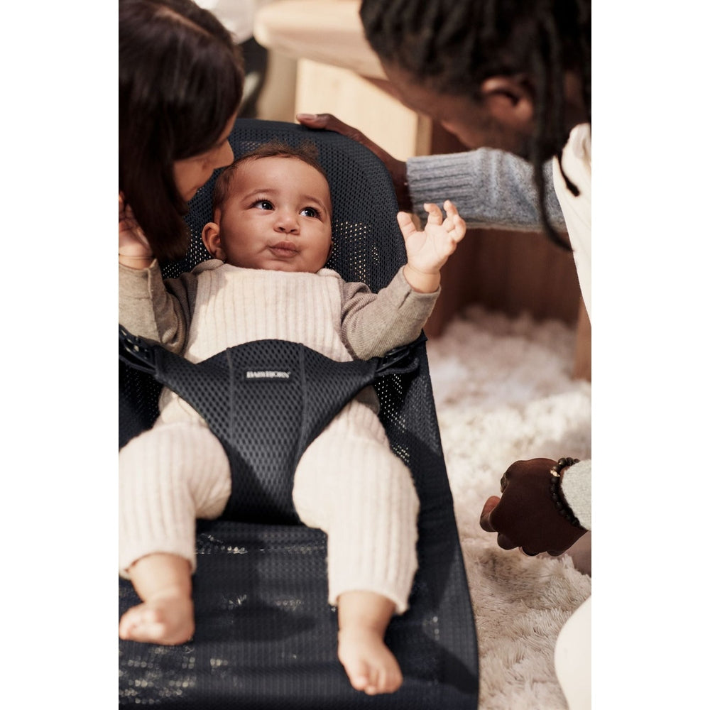 BabyBjorn Bouncer Bliss in breathable mesh, baby smiles with arms out as caregivers lean in.