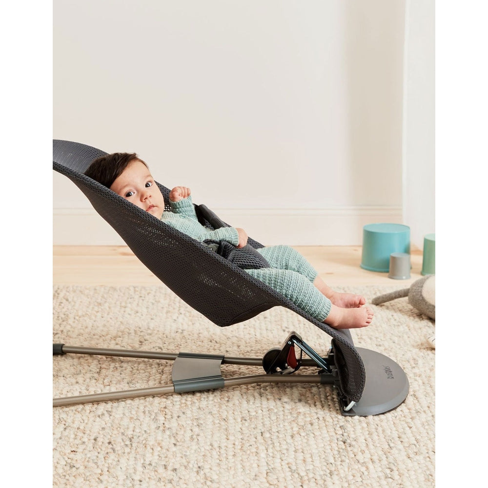 BabyBjorn Bouncer Bliss in dark gray mesh with metal frame; baby reclines in the rocker on a cream carpet.