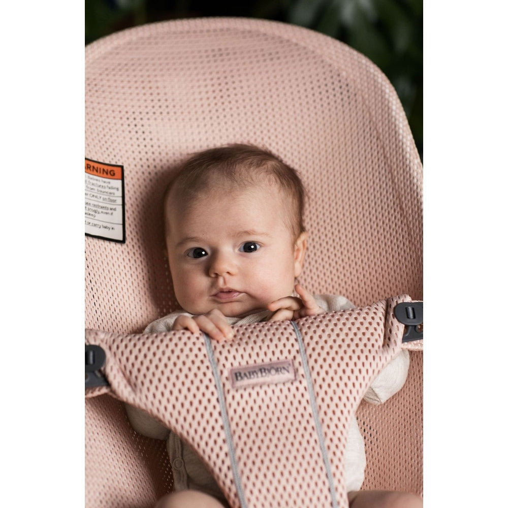 BabyBjorn Bouncer Bliss in pink mesh, breathable seat with brand tag as baby rests hands on the front panel.
