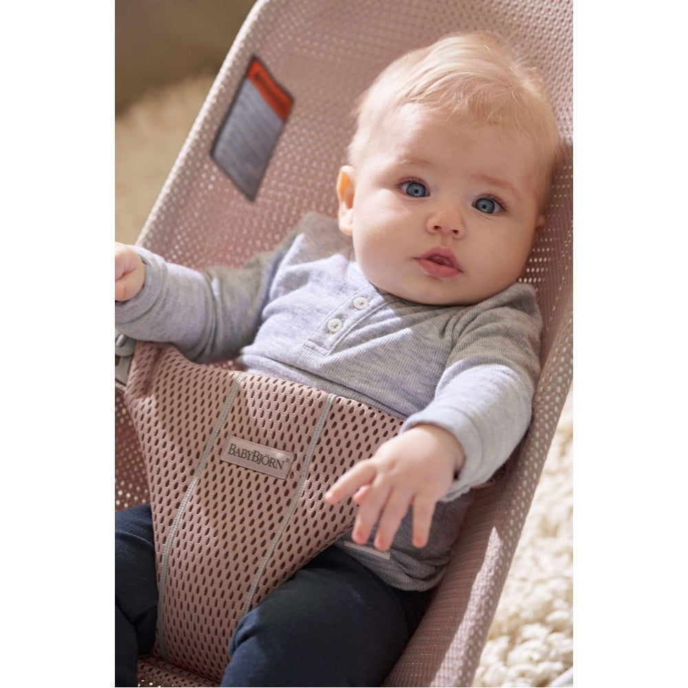 BabyBjorn Bouncer Bliss in soft pink mesh, BABY BJORN, with baby seated and reaching forward.
