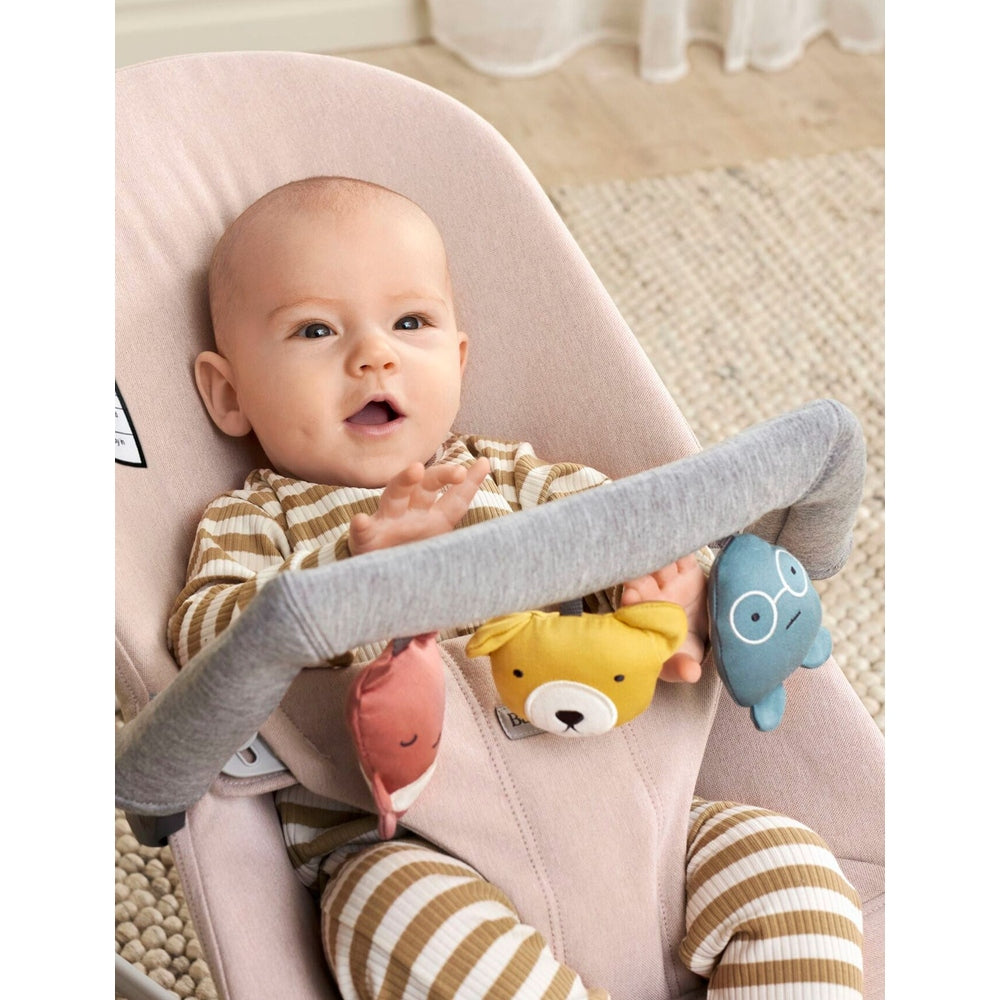 BabyBjorn Baby Bouncer Toy: soft pink seat with gray bar as baby reaches colorful plush toys.