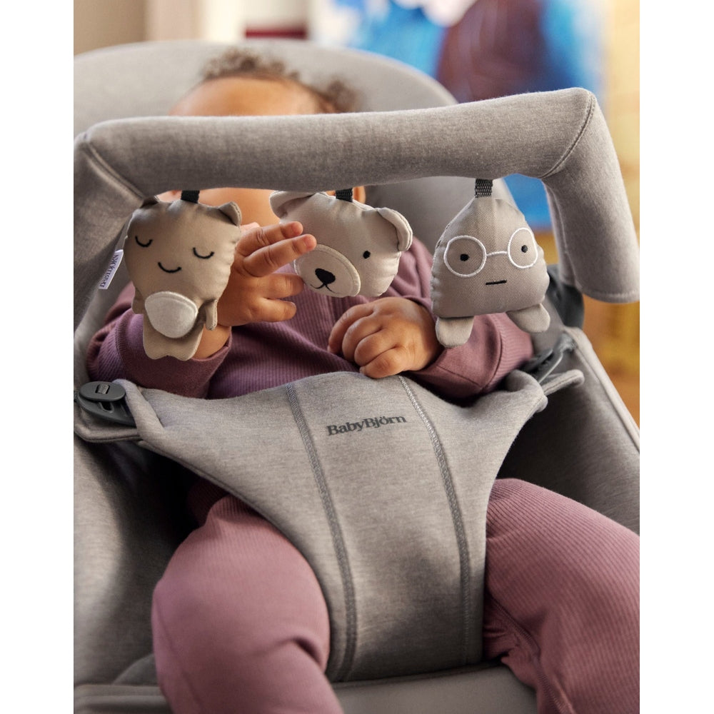 BabyBjorn Bouncer Toy in gray with hanging plush animals; baby reaches for the toys while seated.