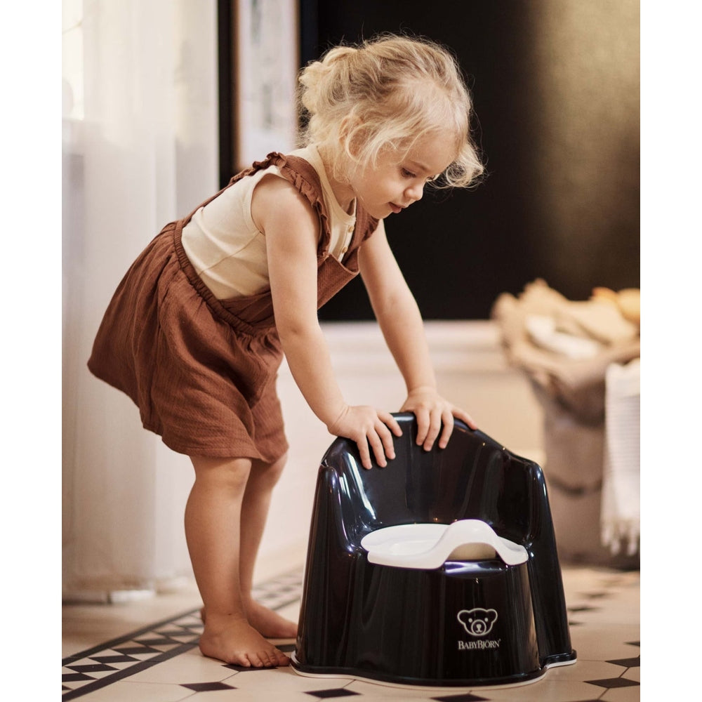 BABY BJORN Potty Chair in black with white insert; a toddler leans over and touches it in the bathroom.