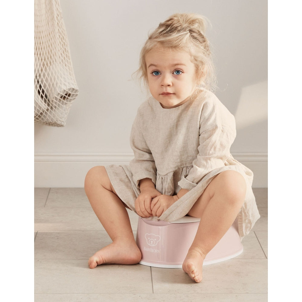 Toddler sitting on a pink BabyBjörn potty in a bright home setting during toilet-learning stage