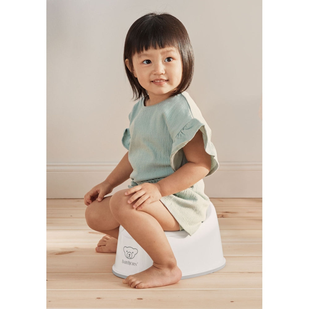 BabyBjorn Smart Potty, white with gray rim, toddler sits on it in a mint dress, demonstrating stability.