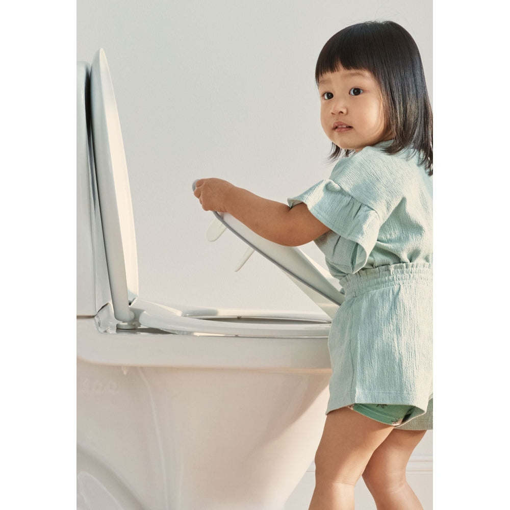 BABY BJORN Toilet Trainer in mint green as a toddler lifts the training seat onto a toilet.