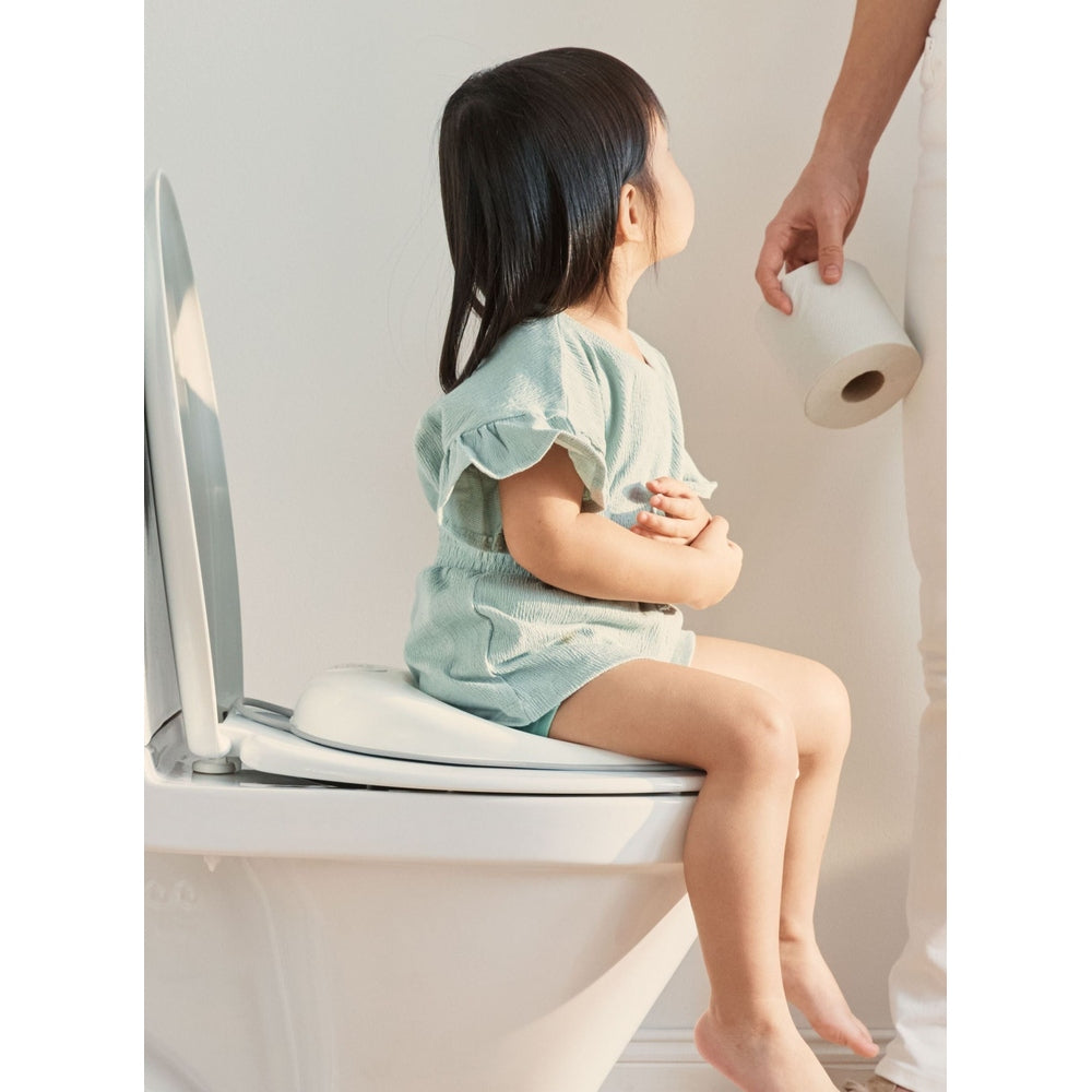 BabyBjorn Toilet Trainer in green; a child sits on the toilet as an adult holds toilet paper.