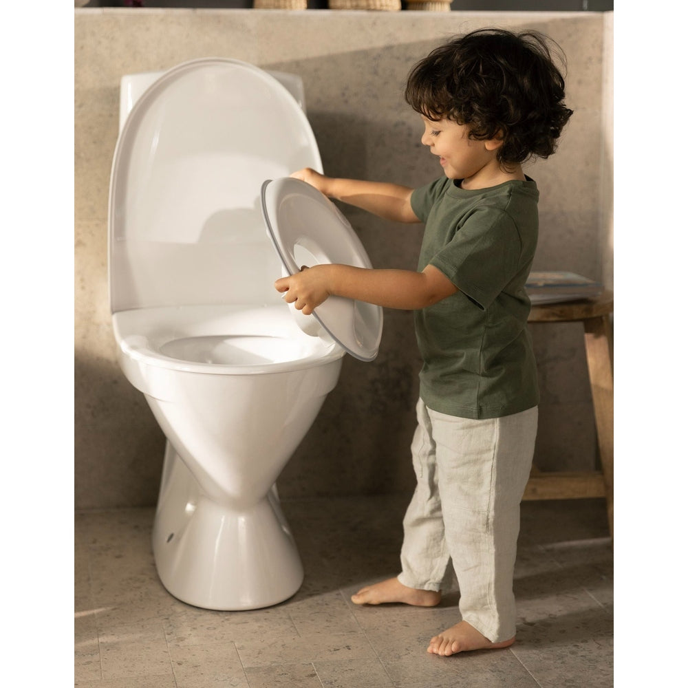 BABY BJORN Toilet Trainer: a toddler lifts the lid on a white toilet, ready to potty train.