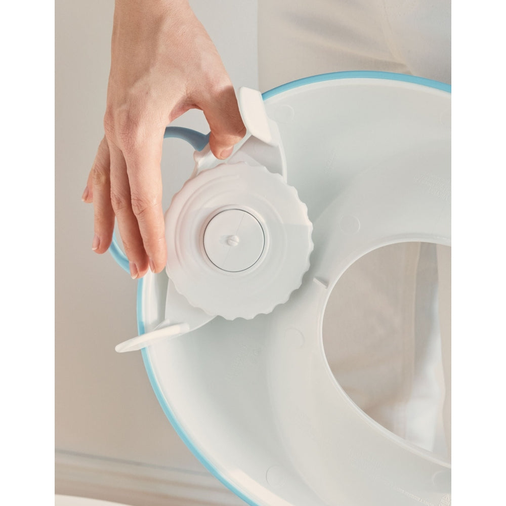 BabyBjorn Toilet Trainer, blue/white, as a parent turns the adjustment dial to secure it.