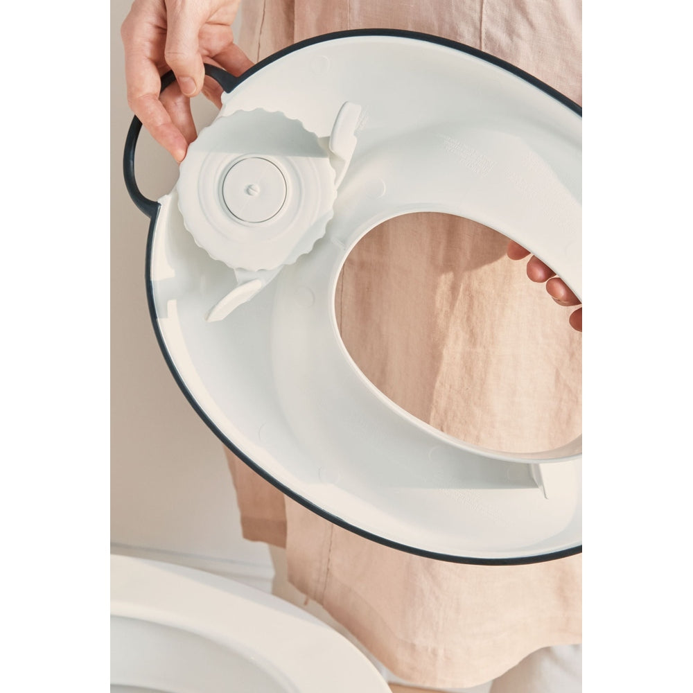 BabyBjorn Toilet Trainer white with navy rim, showing adjustable ring mechanism being held.