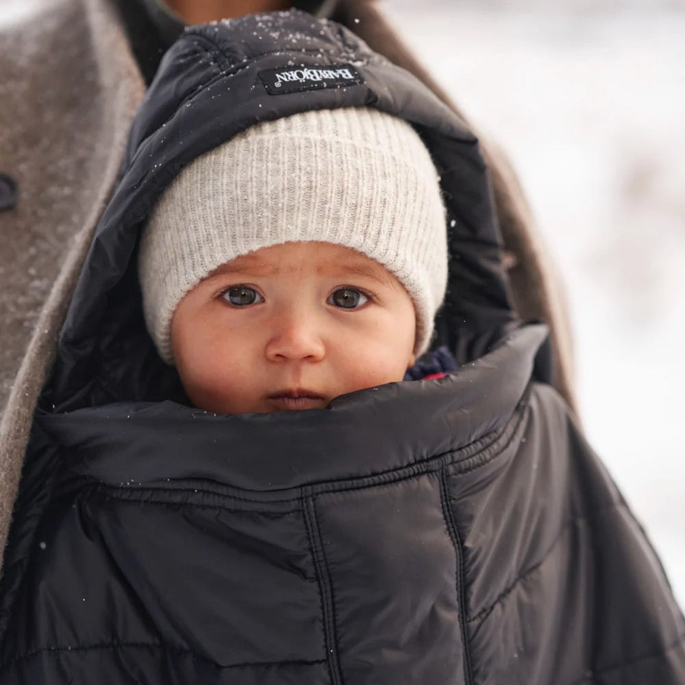 Baby wearing the black BabyBjörn Winter Cover with hood in snowy weather