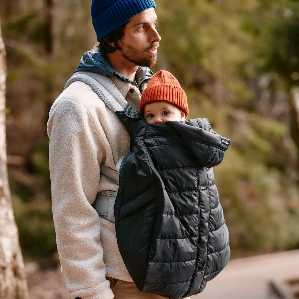 Parent carrying baby outdoors in the black BabyBjörn Winter Cover