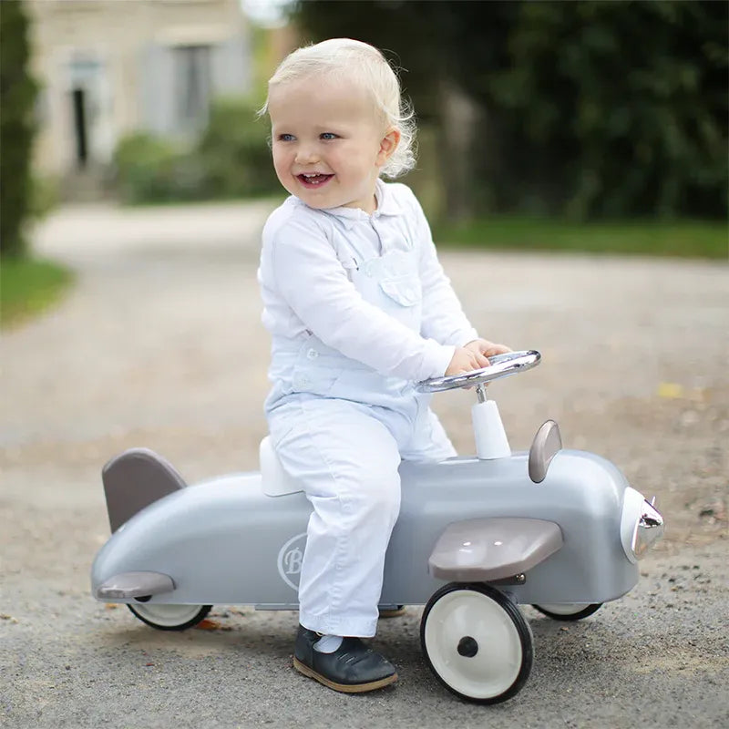 Baghera Ride-On Speedster Plane - Silver, toddler in white steers and rides the retro push pedal toy.