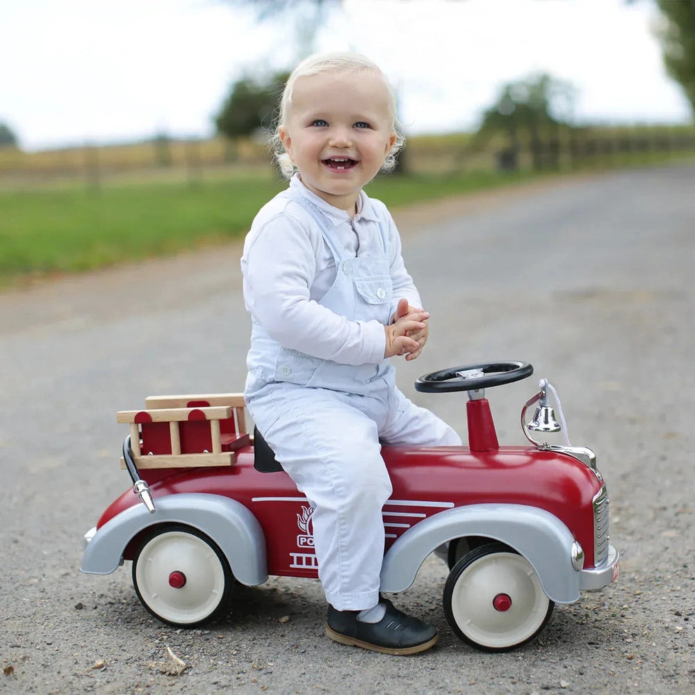 Baghera Ride-On Speedster Car Firetruck; red with gray fenders, toddler sits and steers with a smile.