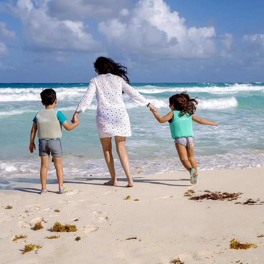 BBLUV Naj Evolutive Neoprene Swim Vest Aqua; a mom leads two kids into the waves, each wearing buoyant aqua vests.