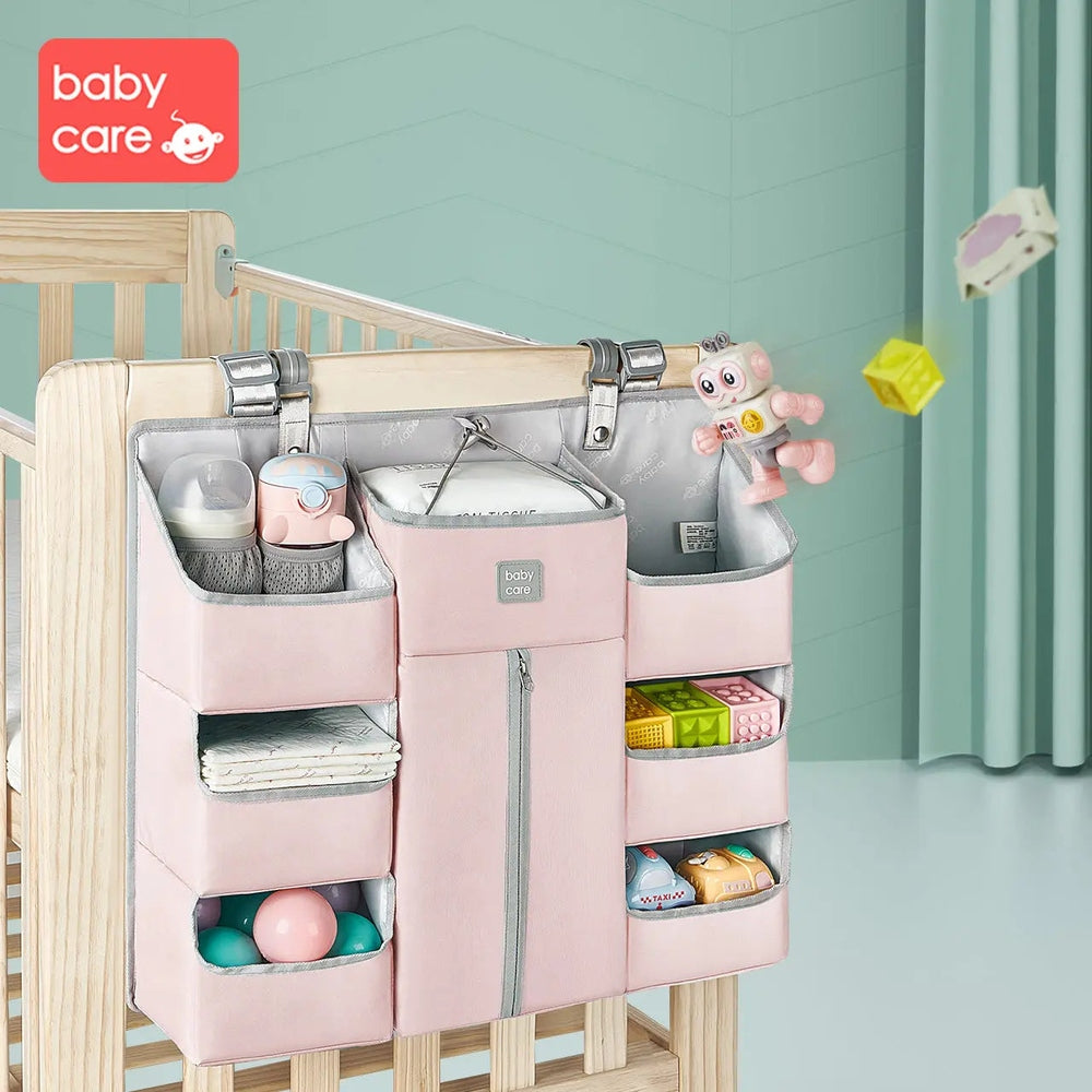 BC Babycare Hanging Storage Bag in pink, hanging from crib rail with labeled pockets storing bottles, toys, and clothes.