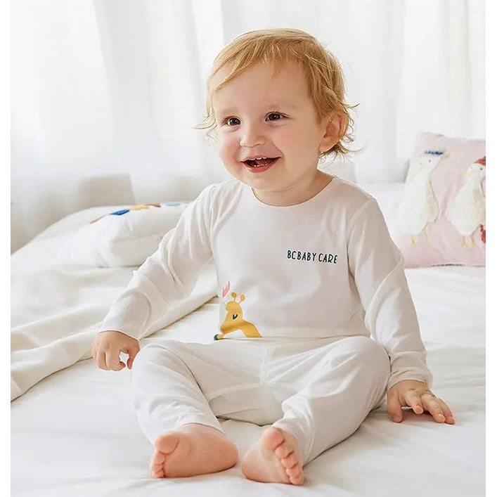 BC Babycare Modal Sleepsuit Cream: baby sits on a white bed in a soft cream long-sleeve sleepsuit.