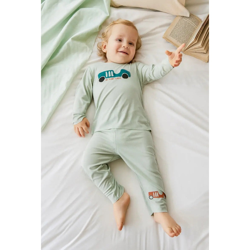 BC Babycare Modal Sleepsuit Green worn by a smiling baby lying on a bed, with car graphic on chest and leg.