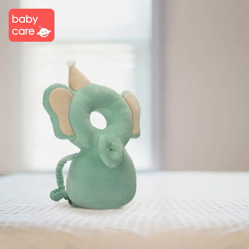 BC Babycare Protective Cushion elephant plush sits upright on a bed, soft green with beige ears.